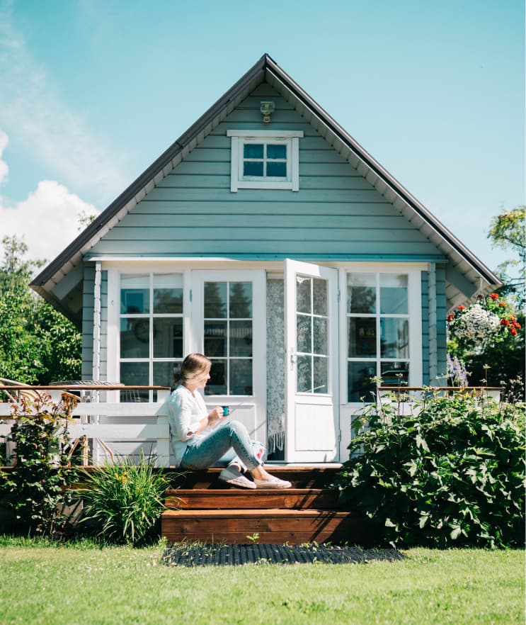 Woman sitting on steps of a house with coffee, representing the home buying journey